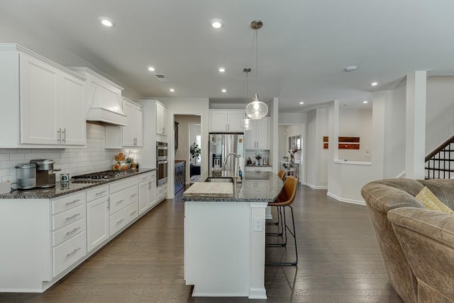 kitchen featuring appliances with stainless steel finishes, a breakfast bar area, dark wood finished floors, backsplash, and custom exhaust hood