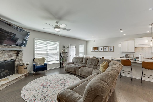 living area featuring a stone fireplace, recessed lighting, dark wood finished floors, and ceiling fan