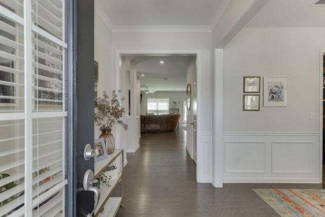 hall with crown molding, a decorative wall, dark wood-style floors, and a wainscoted wall