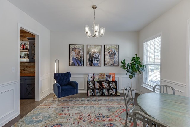 dining space featuring wood finished floors, a decorative wall, a notable chandelier, and a wainscoted wall