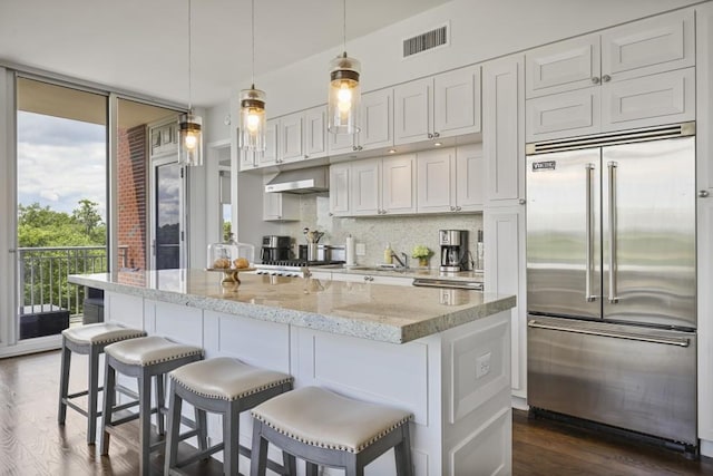 1820 Peachtree St Unit 614, Atlanta, GA 30309 - kitchen featuring built in fridge, under cabinet range hood, a kitchen breakfast bar, white cabinetry, and a center island