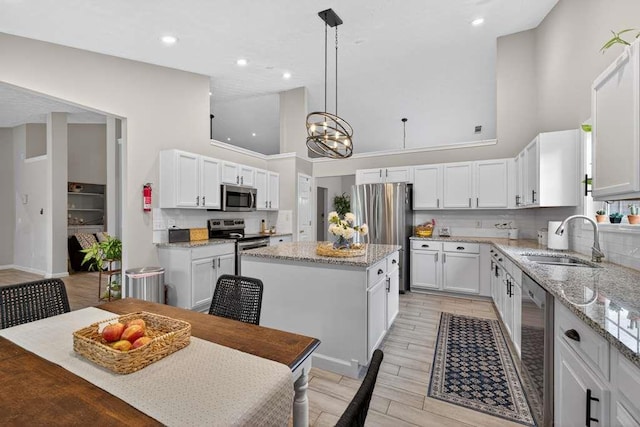 734 Evergreen Dr, Winder, GA 30680 - kitchen featuring high vaulted ceiling, stainless steel appliances, a kitchen island, white cabinetry, and light stone counters