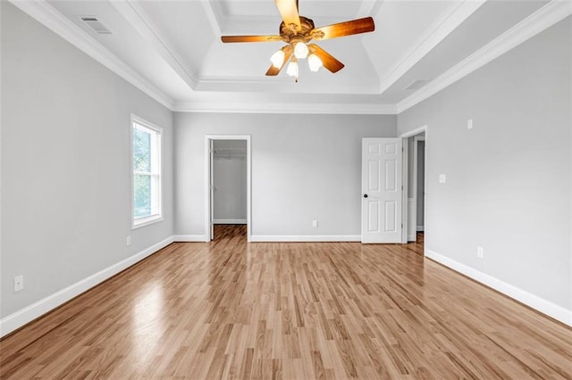 unfurnished bedroom featuring a spacious closet, crown molding, a raised ceiling, light hardwood / wood-style flooring, and ceiling fan