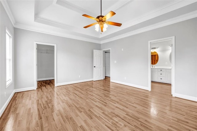 unfurnished bedroom with a walk in closet, ensuite bathroom, ceiling fan, a tray ceiling, and crown molding