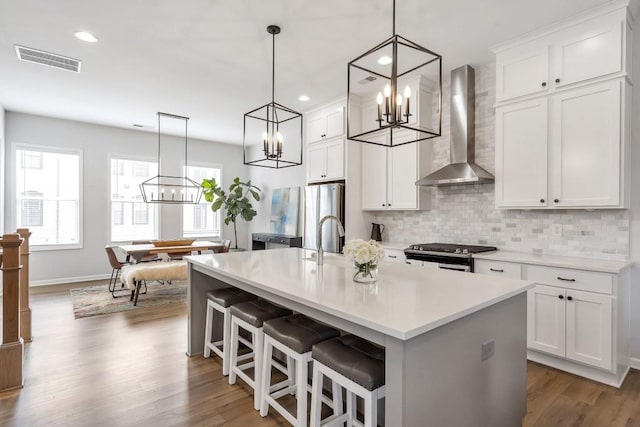 kitchen with wall chimney range hood, stainless steel appliances, white cabinets, and a center island with sink