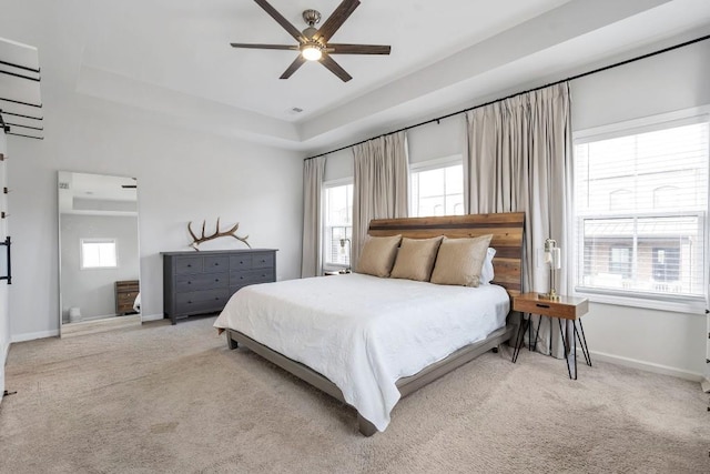 bedroom featuring a raised ceiling, light colored carpet, and ceiling fan