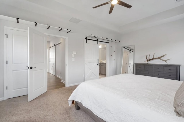 carpeted bedroom with ceiling fan, ensuite bathroom, and a barn door