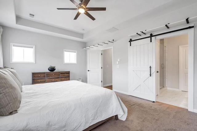 carpeted bedroom featuring a tray ceiling, a barn door, and ceiling fan