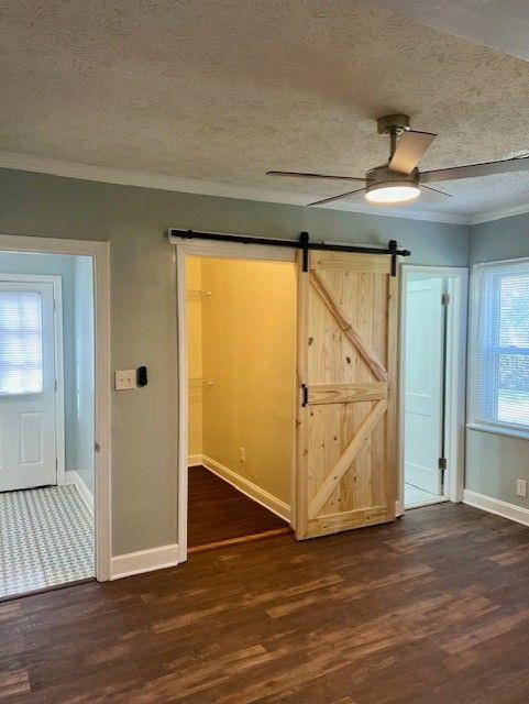 unfurnished bedroom with a barn door, dark wood-type flooring, a textured ceiling, and ceiling fan