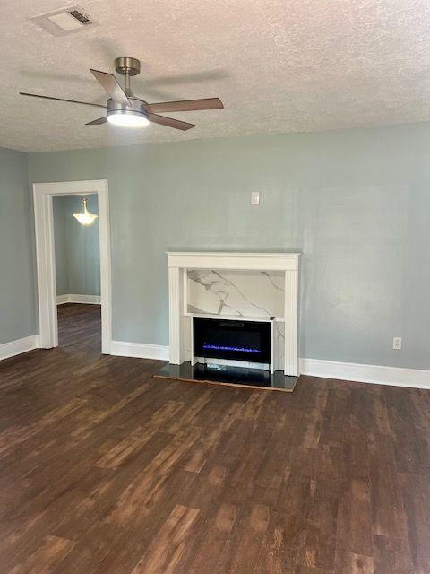 unfurnished living room featuring ceiling fan, a high end fireplace, dark hardwood / wood-style floors, and a textured ceiling