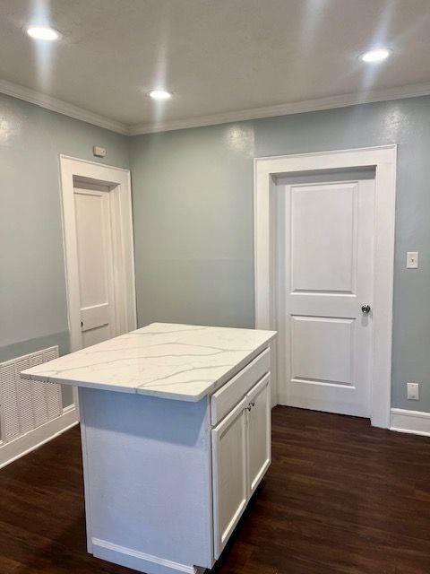 kitchen with white cabinets, dark hardwood / wood-style flooring, a center island, crown molding, and light stone countertops