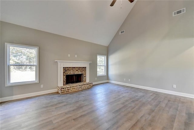 unfurnished living room with ceiling fan, a brick fireplace, hardwood / wood-style floors, and high vaulted ceiling