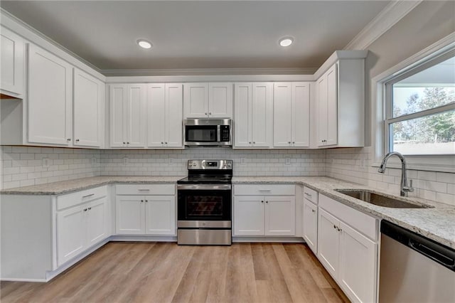 kitchen featuring stainless steel appliances, white cabinets, ornamental molding, sink, and light hardwood / wood-style flooring