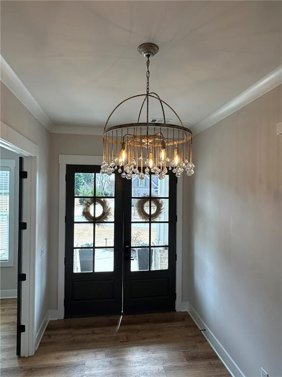 doorway featuring baseboards, wood finished floors, crown molding, french doors, and a notable chandelier