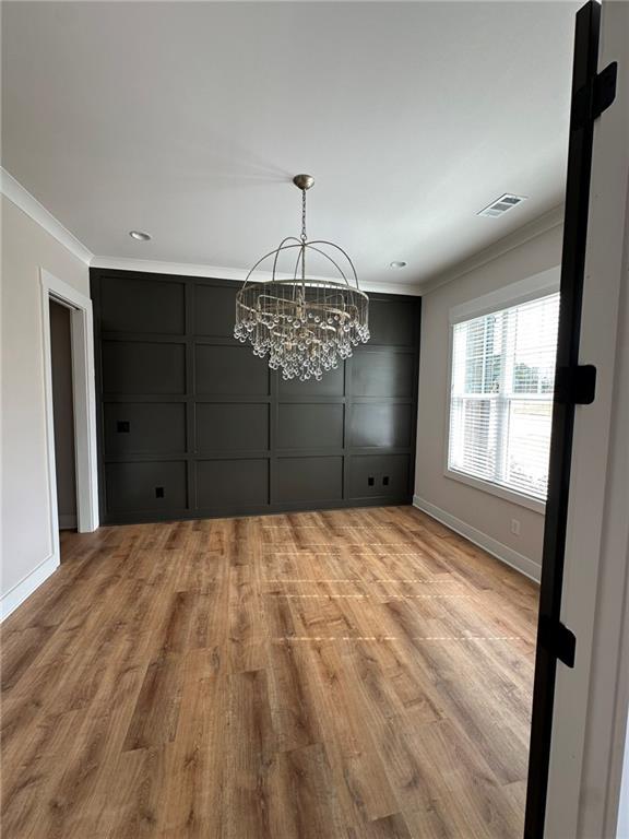 unfurnished room featuring ornamental molding, light wood-style flooring, visible vents, and a decorative wall