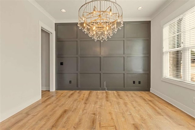 unfurnished dining area with crown molding, wood finished floors, a chandelier, and a decorative wall