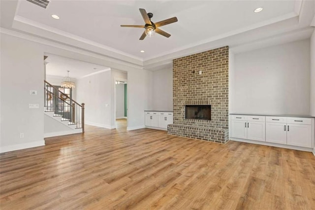 unfurnished living room with a tray ceiling, light wood-style flooring, ornamental molding, a brick fireplace, and baseboards