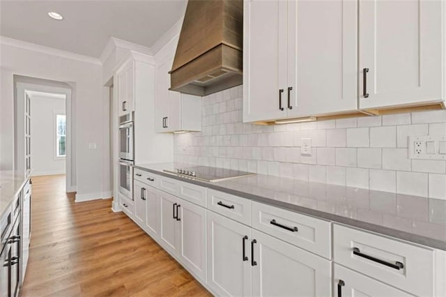 kitchen with crown molding, custom range hood, light wood-style flooring, white cabinetry, and light stone countertops