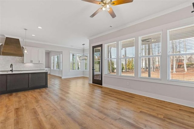 unfurnished living room featuring light wood finished floors, ornamental molding, a ceiling fan, a sink, and baseboards