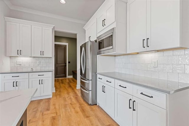 kitchen with light wood finished floors, stainless steel appliances, ornamental molding, and white cabinetry