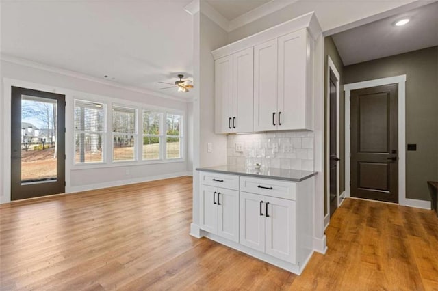 kitchen featuring light wood finished floors, decorative backsplash, ornamental molding, white cabinetry, and baseboards