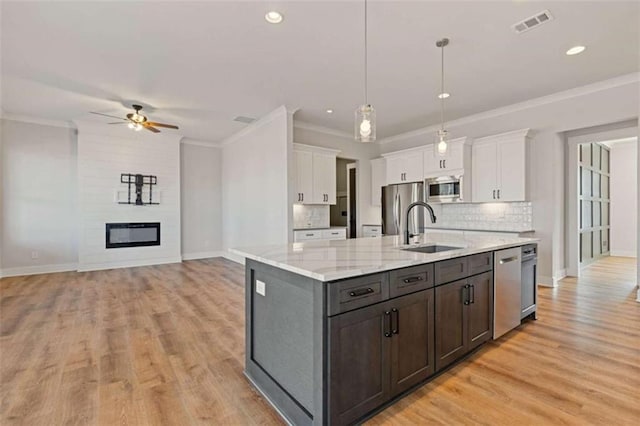 kitchen featuring appliances with stainless steel finishes, ornamental molding, a large fireplace, white cabinets, and a sink