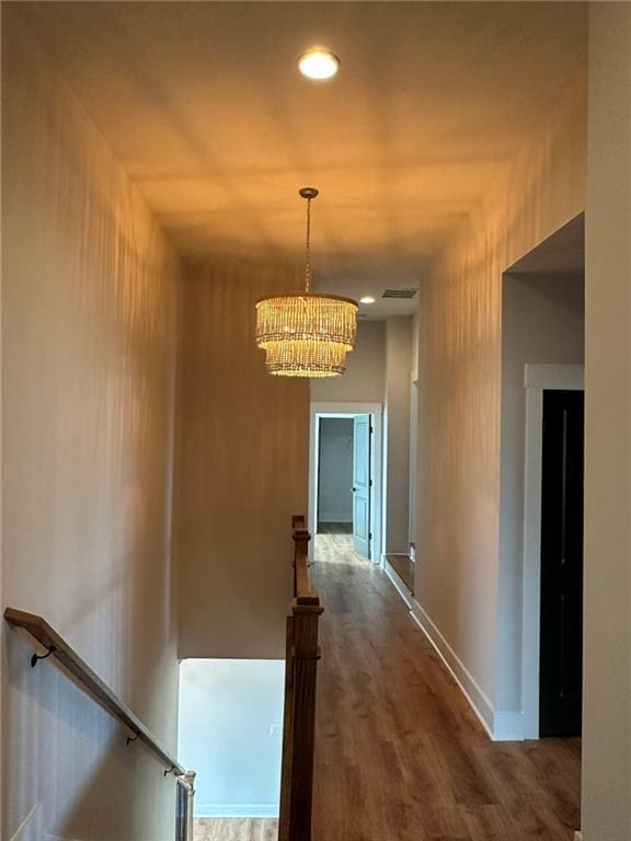 hall featuring visible vents, an inviting chandelier, dark wood-type flooring, an upstairs landing, and baseboards