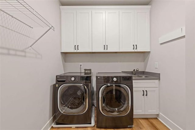 clothes washing area featuring cabinet space, light wood finished floors, baseboards, washer and clothes dryer, and a sink