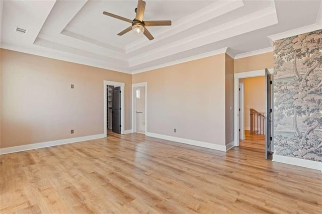 empty room featuring a raised ceiling, visible vents, light wood-style flooring, ornamental molding, and baseboards