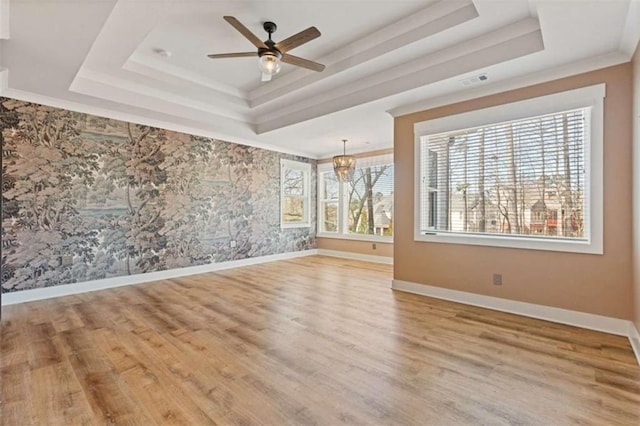 empty room featuring a tray ceiling, baseboards, and wood finished floors