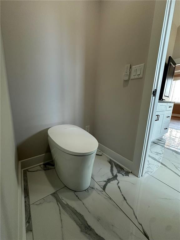 bathroom with toilet, marble finish floor, and baseboards