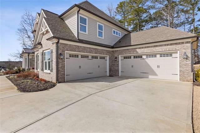 view of property exterior featuring a garage, roof with shingles, concrete driveway, and brick siding