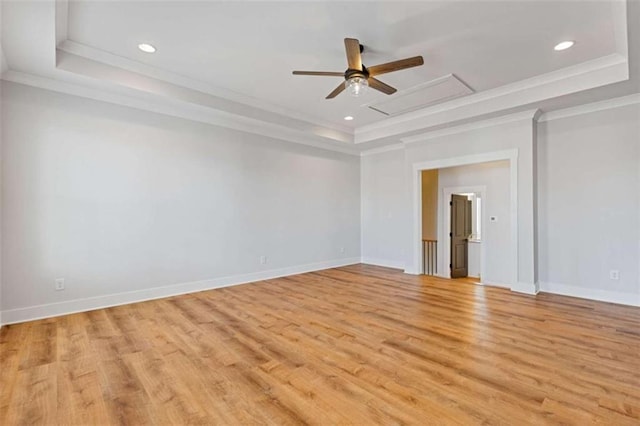 empty room with baseboards, light wood-style flooring, a tray ceiling, crown molding, and recessed lighting