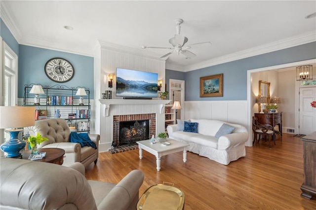 living area featuring visible vents, ceiling fan, ornamental molding, wood finished floors, and a fireplace