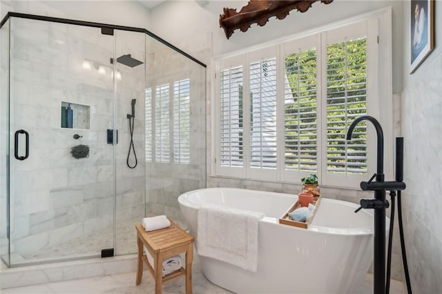 full bath featuring a stall shower, a freestanding tub, a healthy amount of sunlight, and marble finish floor