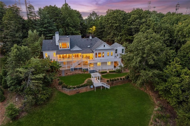 back of property at dusk with a chimney, a lawn, and stairway