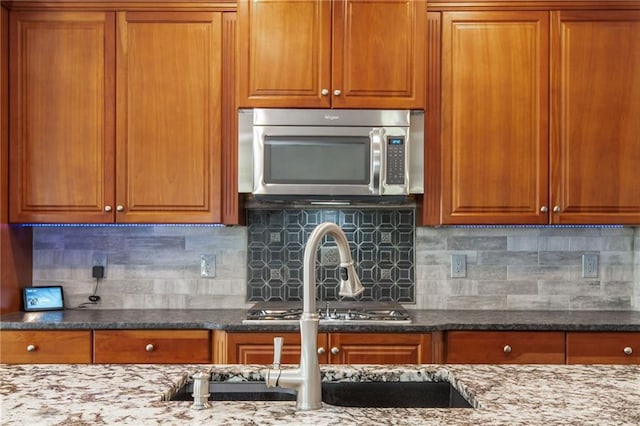 107 Estates At The Lake Dr, Canton, GA 30114 - kitchen with stainless steel microwave, brown cabinetry, backsplash, and dark stone counters