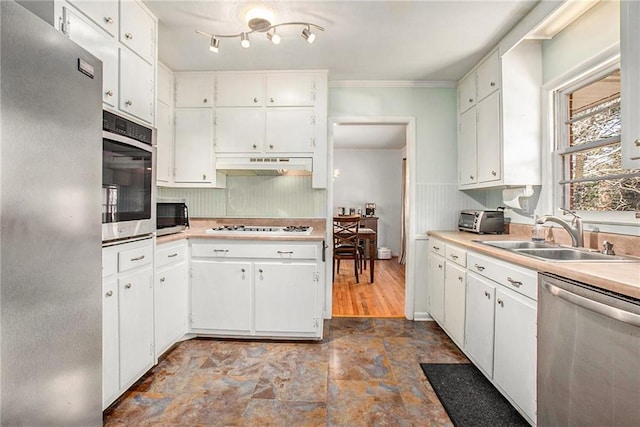 kitchen with light countertops, appliances with stainless steel finishes, white cabinets, a sink, and under cabinet range hood