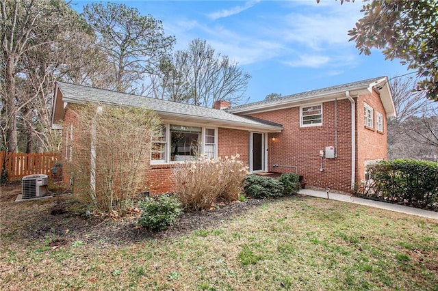 tri-level home featuring brick siding, a chimney, central AC unit, a front yard, and fence