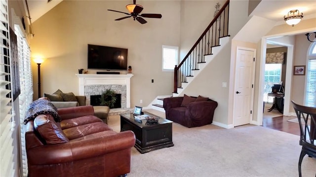 carpeted living room featuring a stone fireplace, stairway, baseboards, and a healthy amount of sunlight