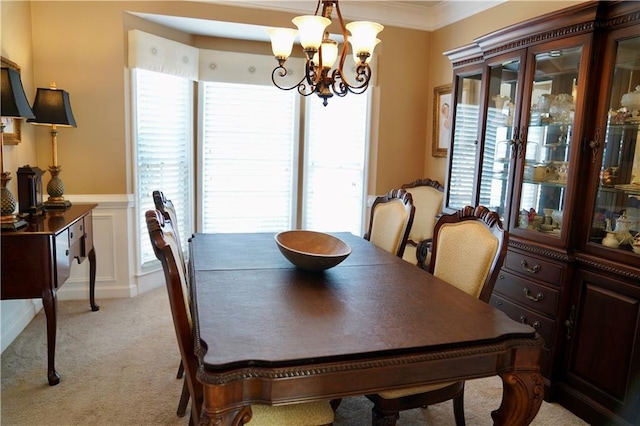 dining space featuring a wainscoted wall, a notable chandelier, crown molding, a decorative wall, and light colored carpet