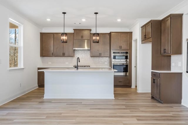 kitchen with double oven, light countertops, decorative light fixtures, and under cabinet range hood