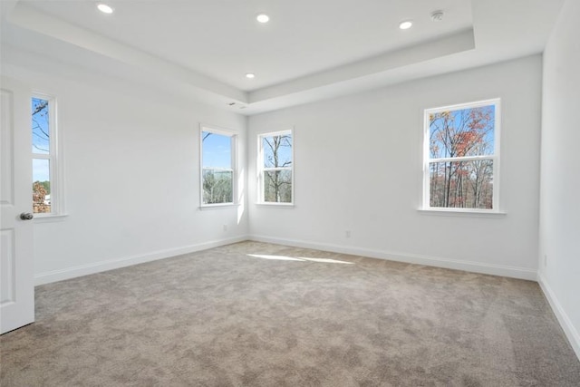 empty room featuring light carpet, a tray ceiling, recessed lighting, and baseboards