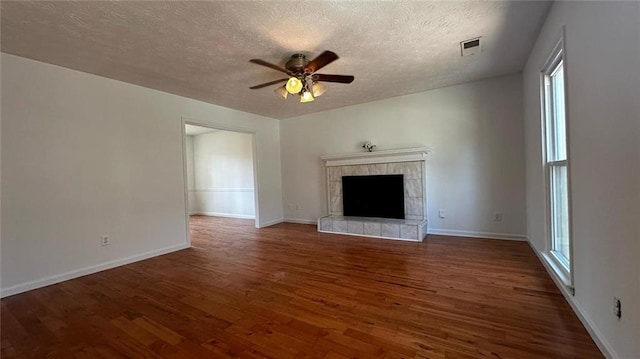 unfurnished living room with plenty of natural light, a ceiling fan, wood finished floors, and a tiled fireplace