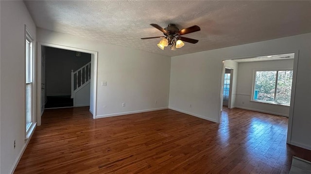 empty room featuring ceiling fan, baseboards, stairs, wood finished floors, and a textured ceiling