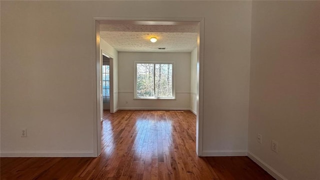 unfurnished room featuring a textured ceiling, baseboards, and hardwood / wood-style flooring