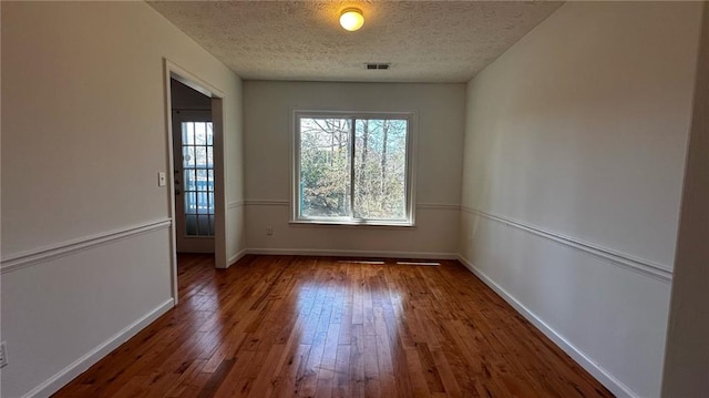 empty room with visible vents, wood-type flooring, a textured ceiling, and baseboards