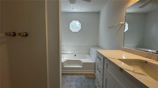 bathroom with a garden tub, vanity, a textured ceiling, and a ceiling fan