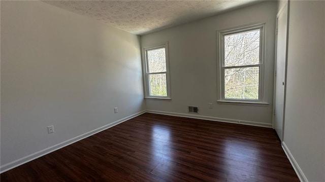 unfurnished room with visible vents, a textured ceiling, dark wood-type flooring, and baseboards