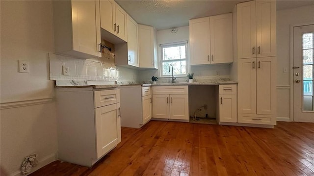 kitchen featuring a sink, backsplash, hardwood / wood-style floors, and white cabinetry